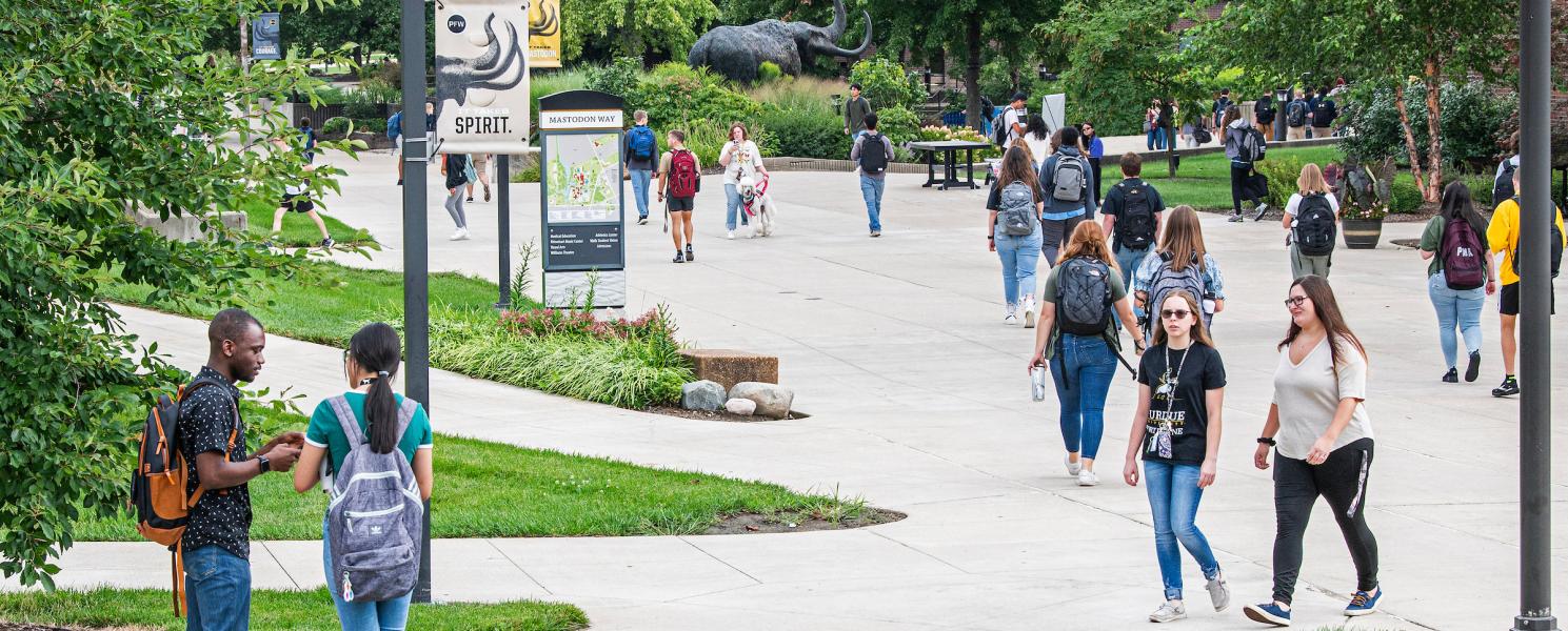 Students walking outside on campus with the Mastodon Statue in the background.