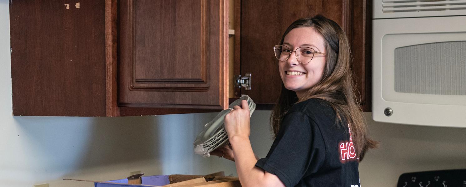 Student putting plates in the cabinet while moving in to Student Housing.