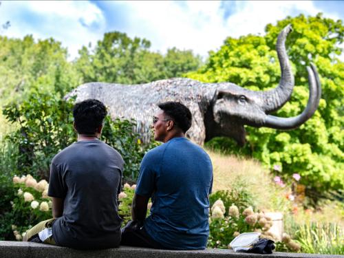 Two students site on a ledge near the Mastodon statue.