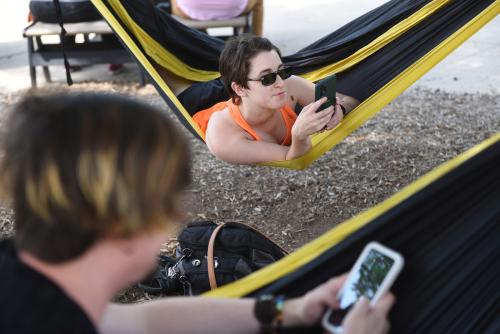 Students on their phones outside as they lounge in hammocks on campus.