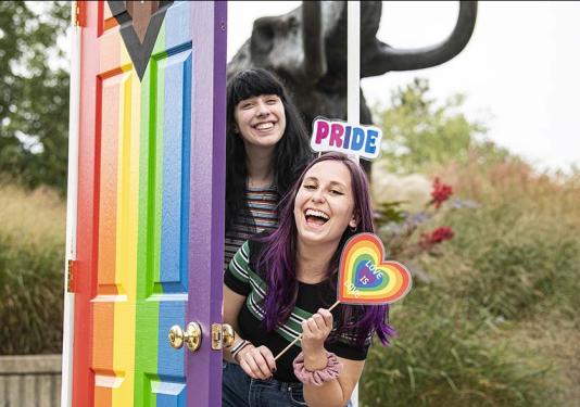Two students are coming out of a rainbow-painted photo booth in celebration of National Coming Out Day.