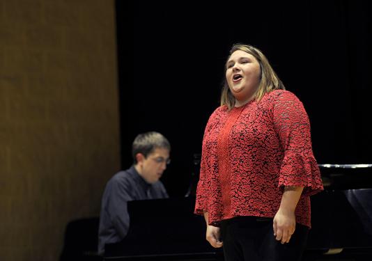 A woman stands and sings in front of a black background.