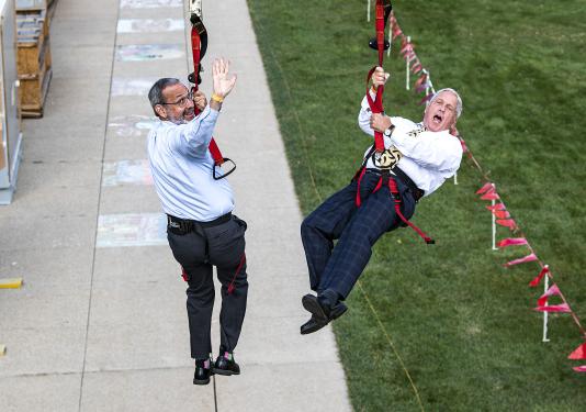 Deans Ron Friedman and John O'Connell head down the zipline at the annual Dons Picnic on the Lawn