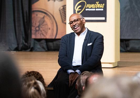 Omnibus speaker Michael Steele sits on the edge of the stage in Auer Performance Hall.