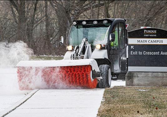 A grounds crew member is brushing the snow off of the sidewalk