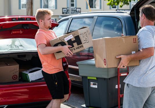 A student moves boxes in with a parent on move-in day.