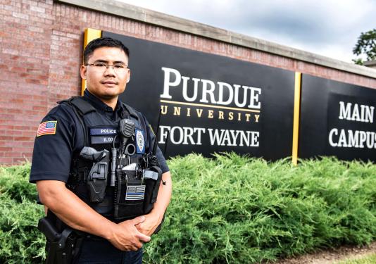 PFW police officer Htoo Doh is standing in front of the Purdue Fort Wayne main campus sign