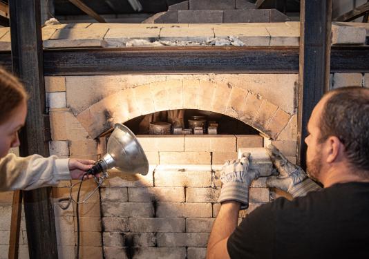 Two people are loading a wood burning kiln
