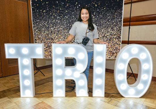 Aurea Alconera is standing behind a large TRIO lighted sign.