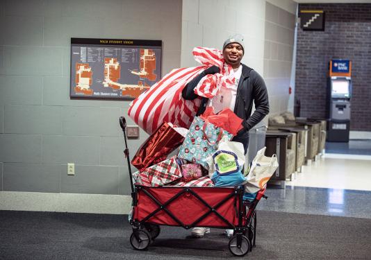 A man is standing beside a cart full of holiday gifts