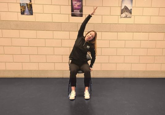 Chair yoga instructor showing how to do a side stretch shair yoga pose.