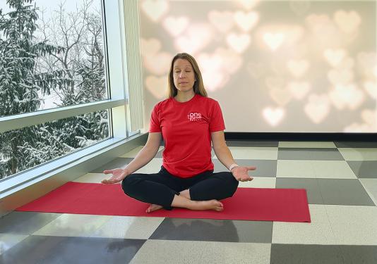 Yoga instructor in red t-shirt for Healthy Heart month showing the seated meditation pose.