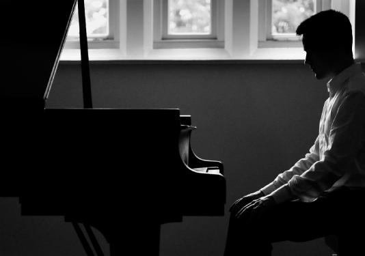 man sitting at piano in black and white