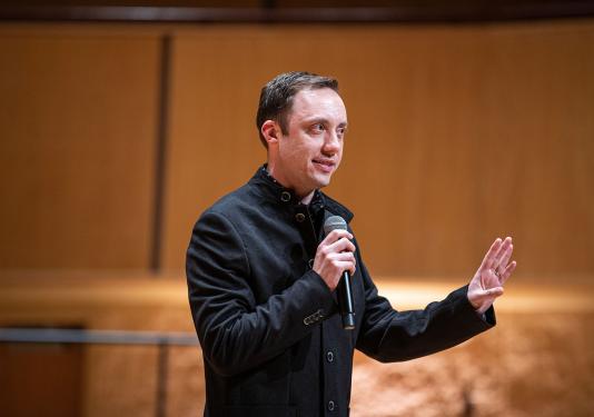 William Sauerland is onstage and speaking with a microphone