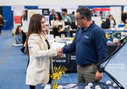 A student is shaking hands with a prospective employer at a career fair