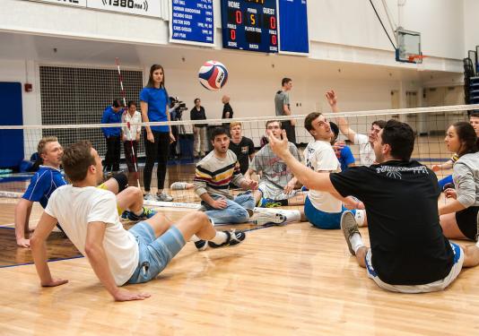 Two teams are playing volleyball while sitting down