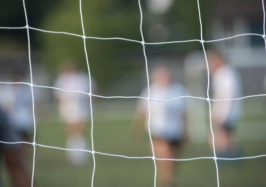 Soccer players seen through a goal net