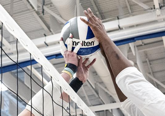 Two volleyball players are reaching for a volleyball