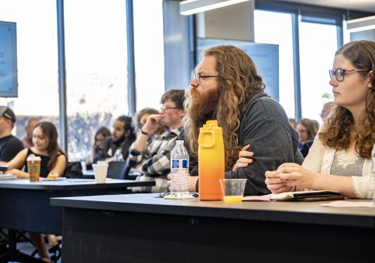 Students sitting at tables listening to a presenter.