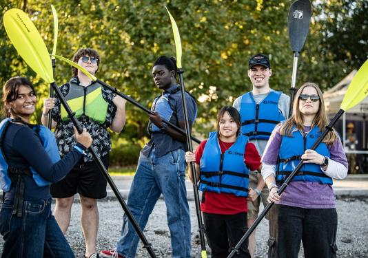 Several students are holding kayak paddles
