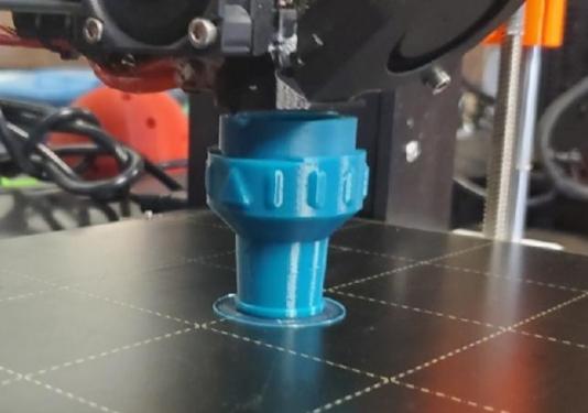 A hose adapter is pictured here in the 3D printer.