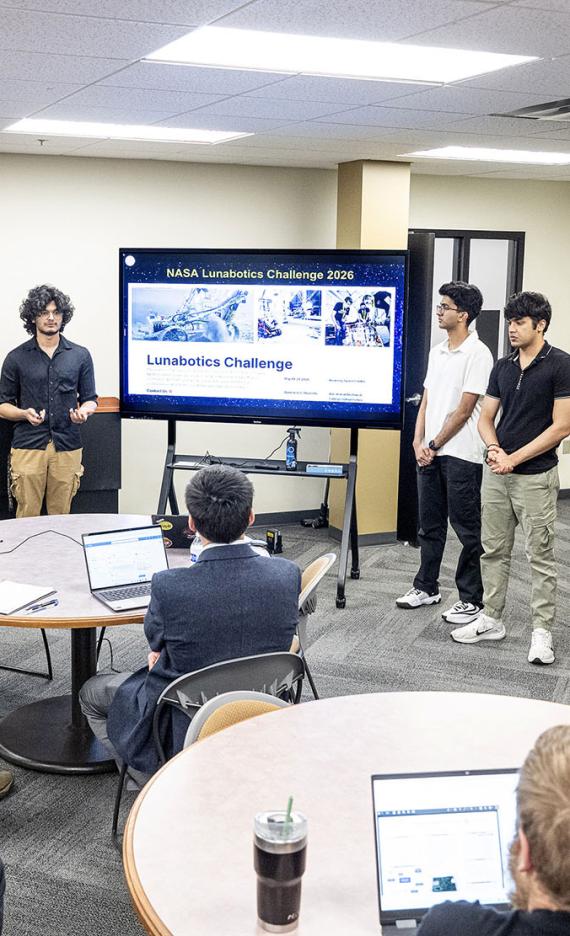 Members of the Lunarbotics team are lined up next to a large video display