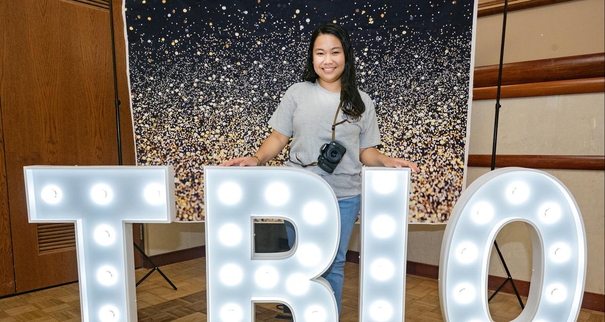 Aurea Alconera is standing behind a large TRIO lighted sign.