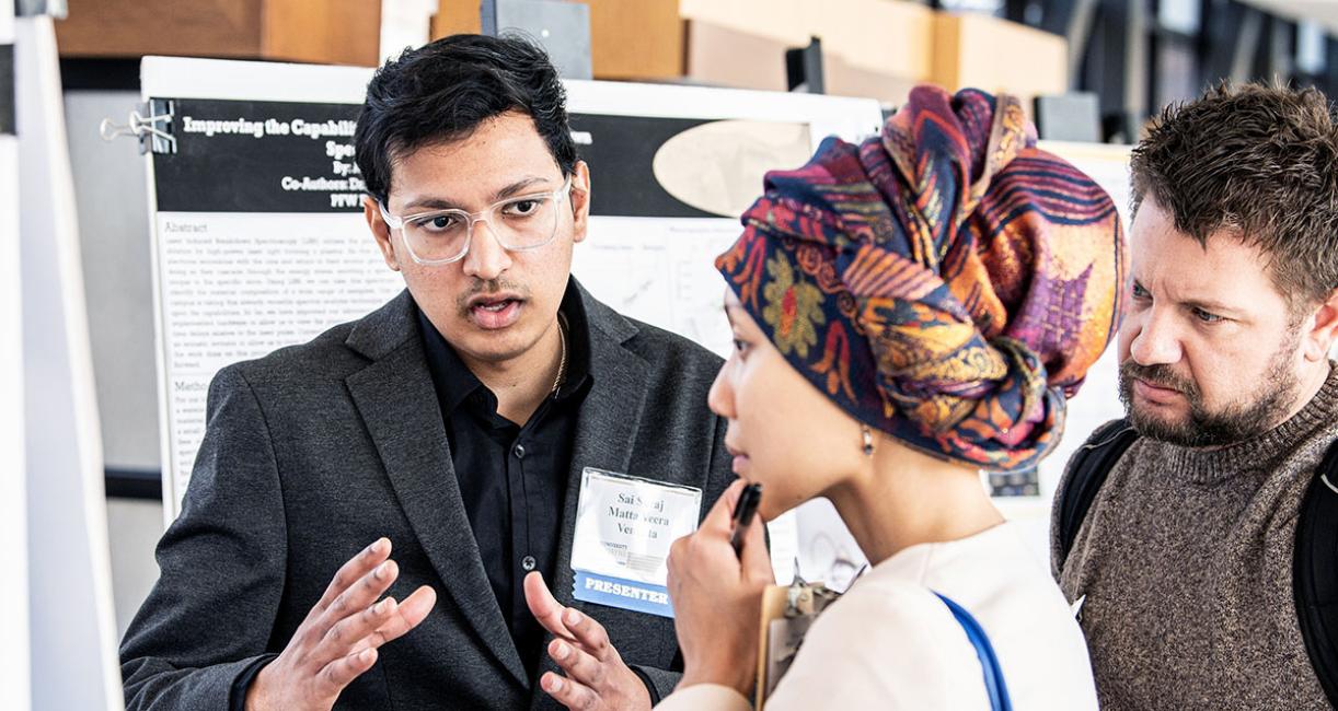 A student explains his research project to a judge at the symposium