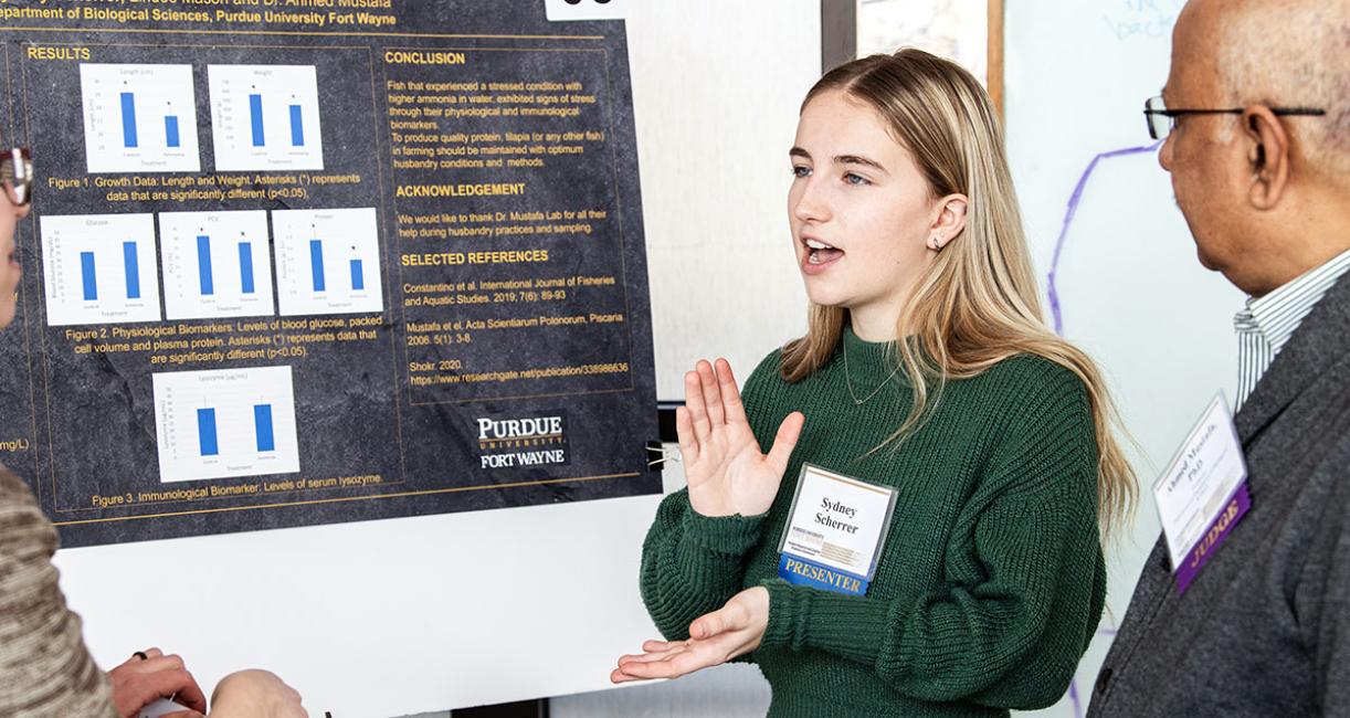A student explains her research project to a judge at the symposium