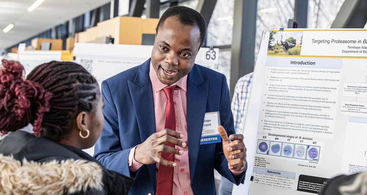 A student explains his research project to a judge at the symposium