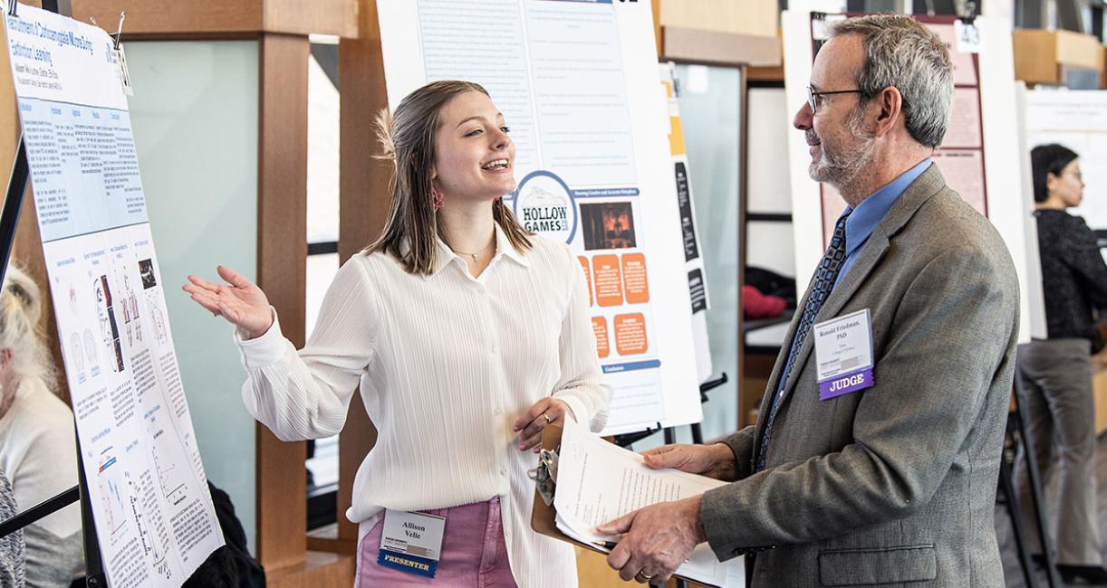 A student explains her research project to a judge at the symposium