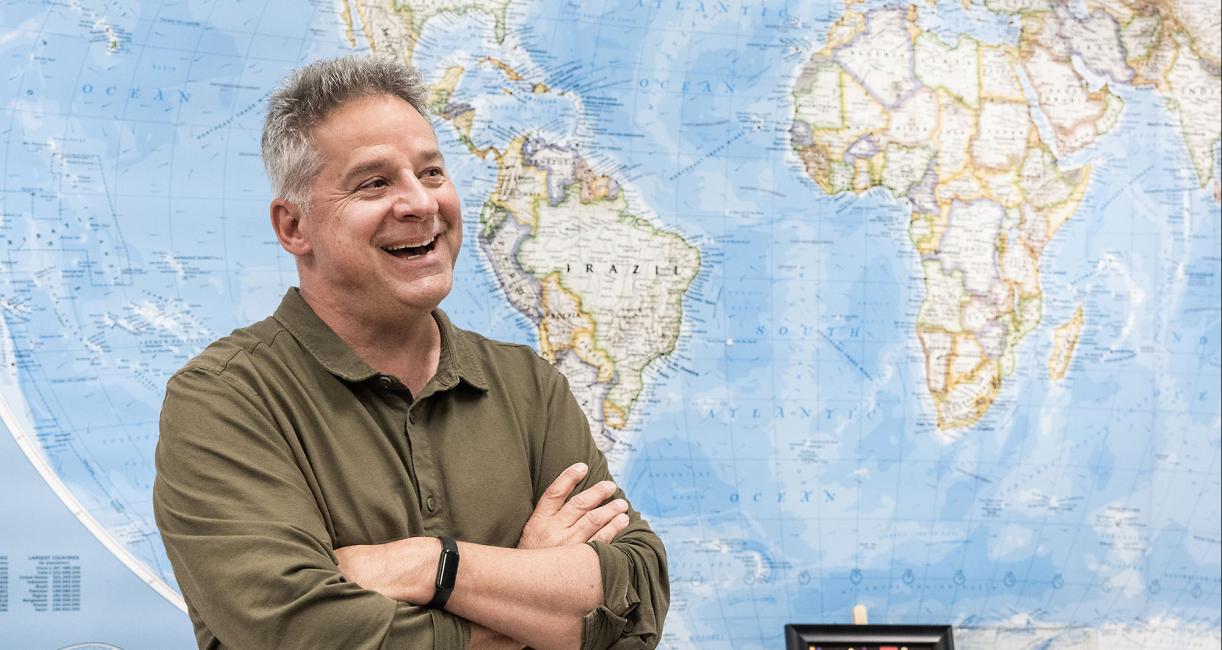 John Jensen is standing in front of a map of the world.