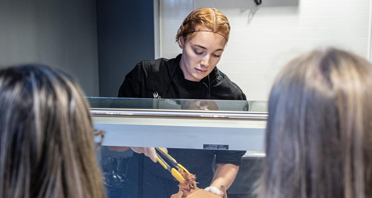A food service worker is adding food to a box