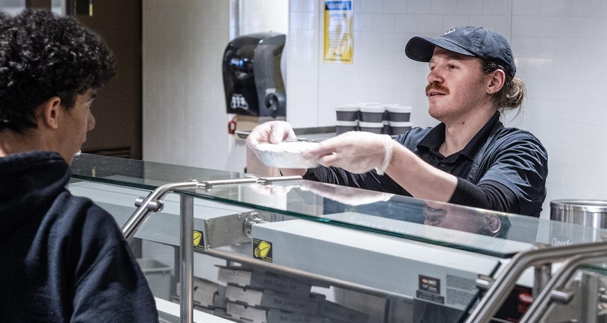 A food service worker is handing a bowl to a student
