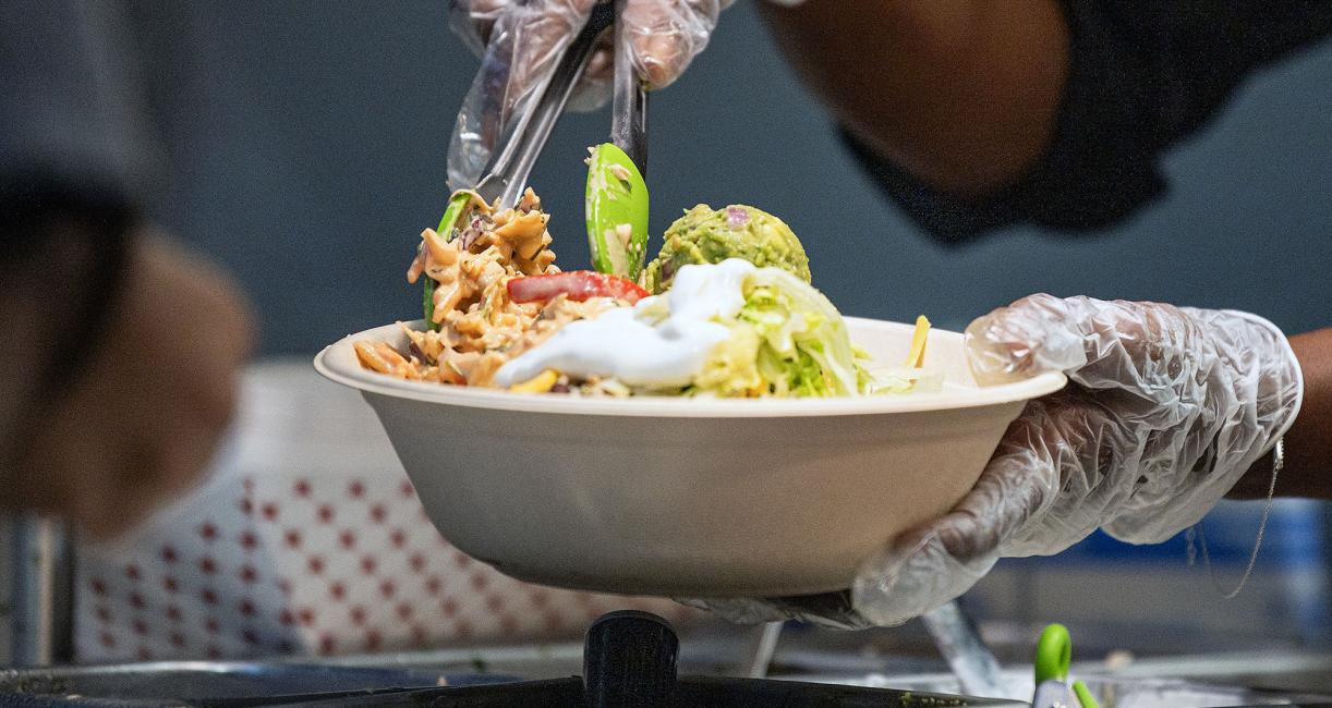 A food service worker is building a taco salad