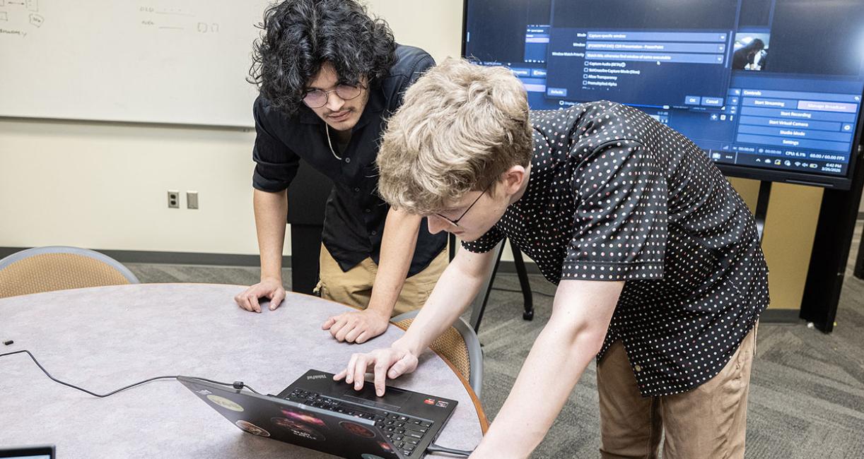 Two students are leaning over a computer