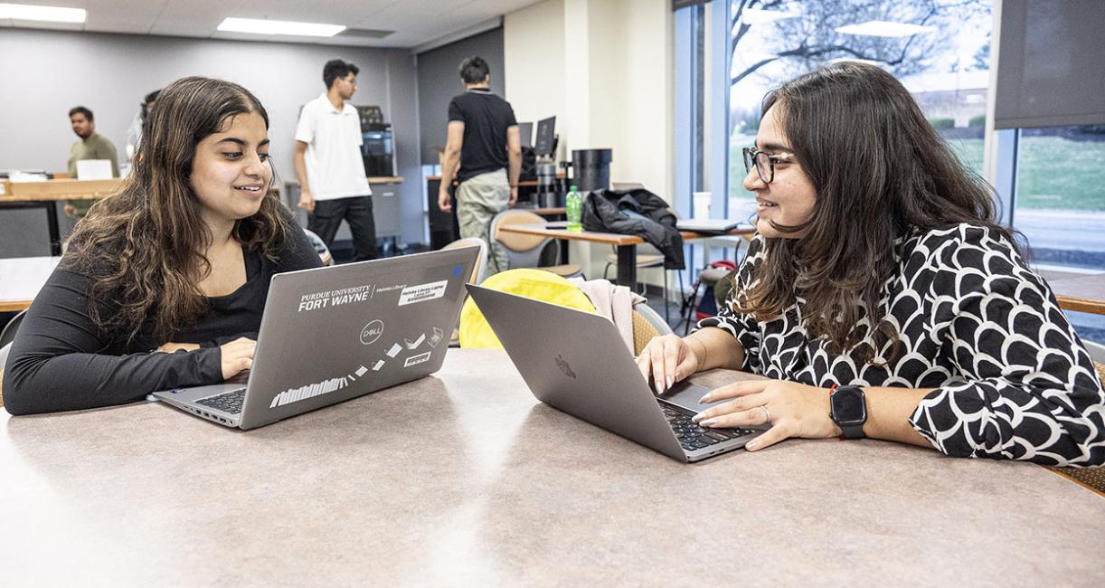 Two students are working at their computers and looking at each other