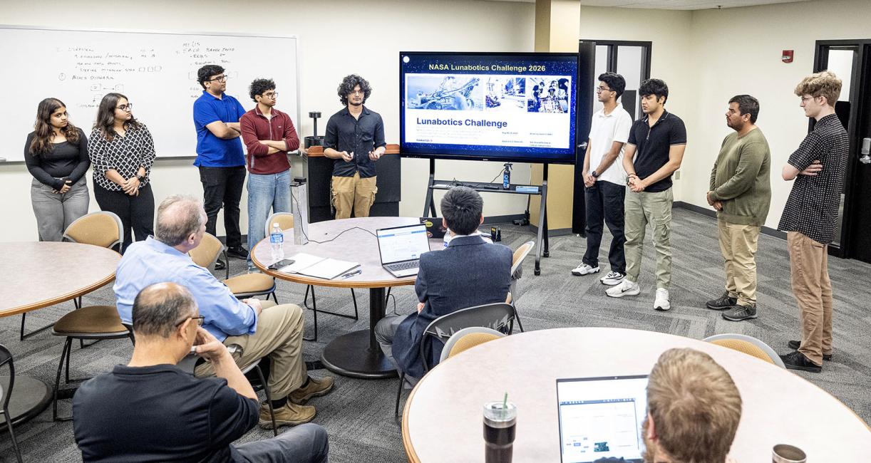 Members of the Lunarbotics team are lined up next to a large video display