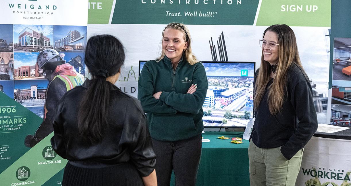 Two representatives of construction companies are speaking to a conference attendee