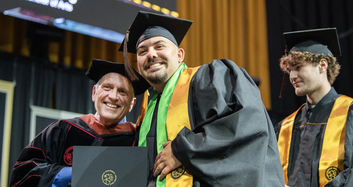 A student and faculty member pose with a degree at the 2026 commencement ceremony
