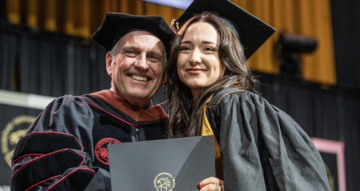 A female student and faculty member pose with a degree at the 2026 commencement ceremony
