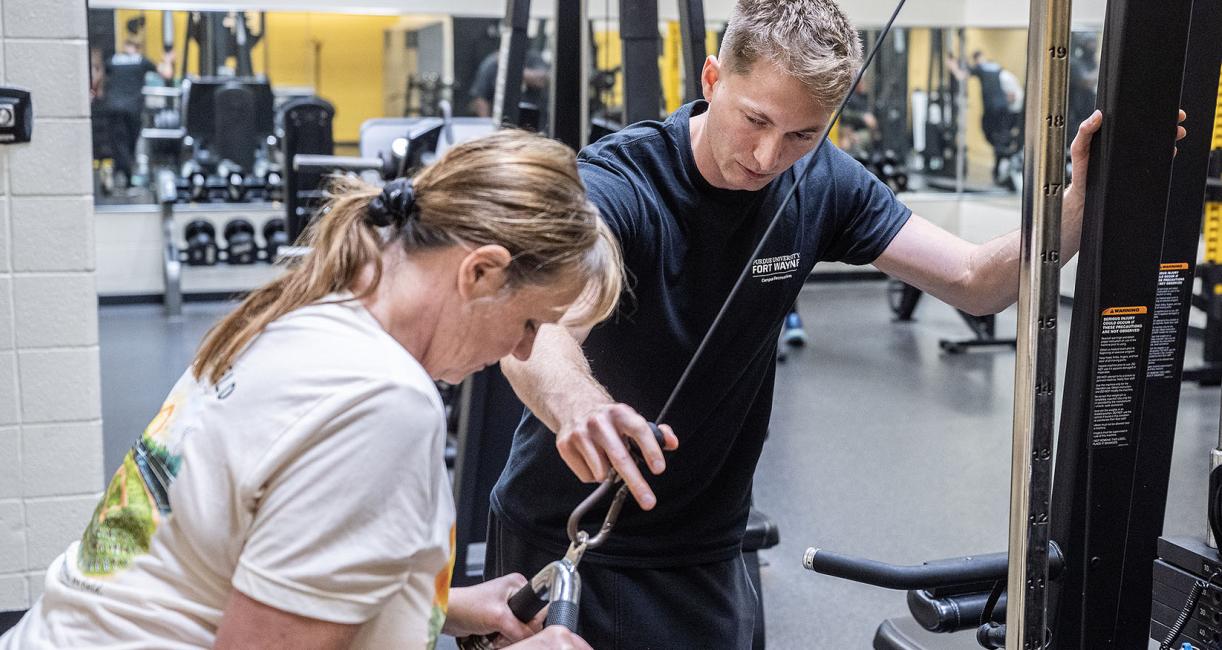 A trainer is assisting a student in a gym