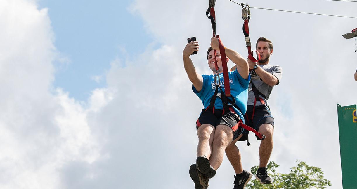 Two students are riding zipline while taking a selfie